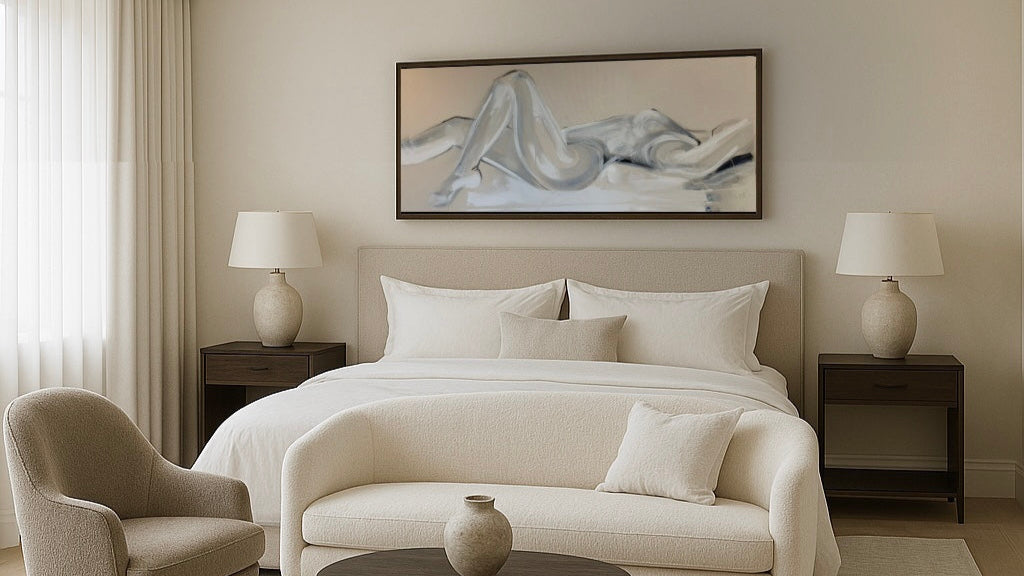 lying down woman figurative painting in white and grey tones. Monochrome painting painted by artist Briony May Richardson at Studio BMR. Situated within a neutral bedroom decor with stone coloured interior design aspects such as a headboard, accent chair and ceramics.  Two oversized bedside lamps and a dark wood finished bedside tables.