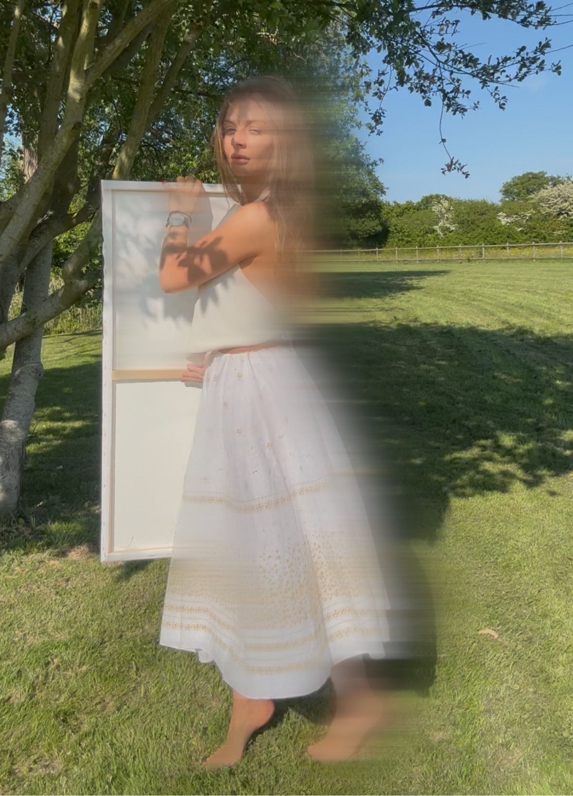 Uk and essex artist Briony May Richardson in the garden of StudioBMR. Holding a canvas painting of hers taken in a creative photographic style.